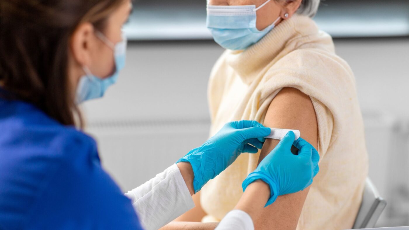 Eine Apothekerin klebt einer Patientin einen Pflaster auf.