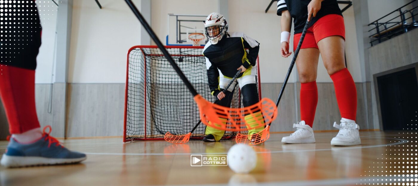 Drei Menschen spielen zusammen Floorball in einer Sporthalle