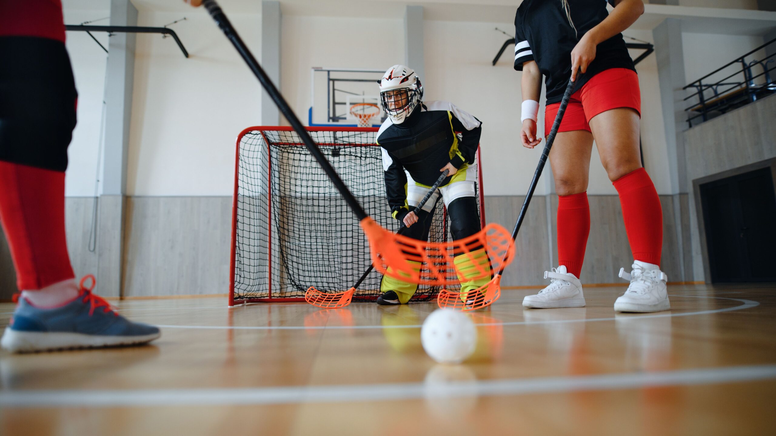 Drei Menschen spielen zusammen Floorball in einer Sporthalle