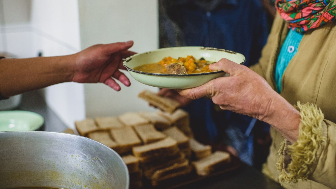 Eine Frau gibt einem anderen Menschen einen Teller mit warmer Suppe