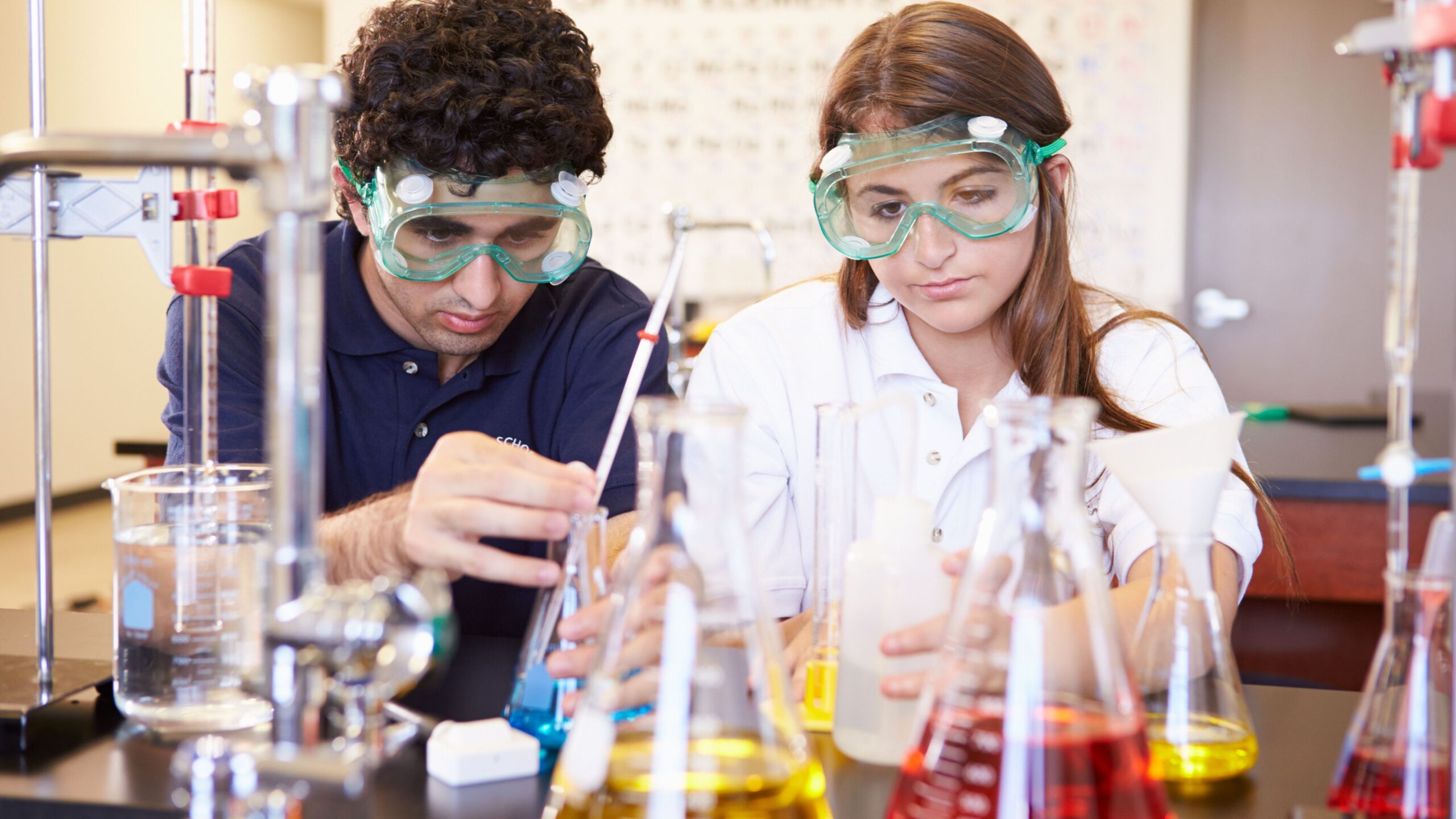 ein Junge und ein Mädchen sitzen vor mehreren Reagenzgläsern und Chemiebehältern mit Flüssigkeiten in einem Labor