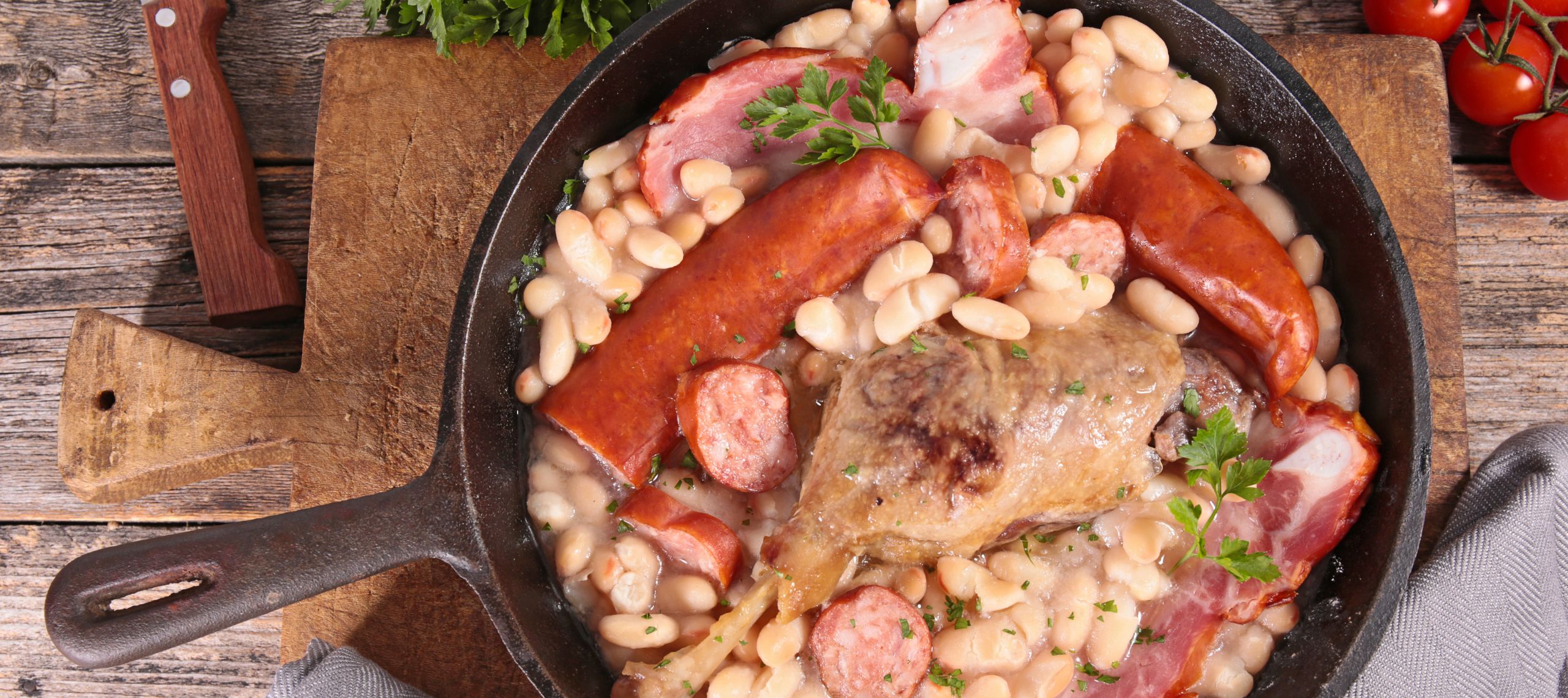 Ein angerichtetes Bohnencassoulet aus Südfrankreich mit weißen Bohnen, Speck, Kassle r und einem Hähnchenflügel in einer gusseisernen Pfanne