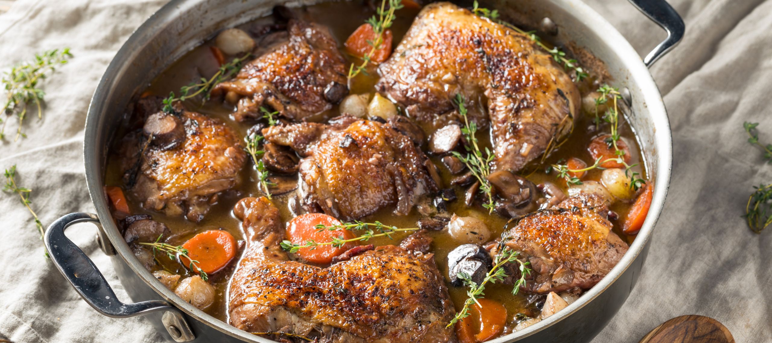 In einer Pfanne ist frisches Coq au Vin aus der französischen Küche mit Quarkknöpfle aus der Lausitzer Küche frisch aus dem Ofen schmackhaft angerichtet