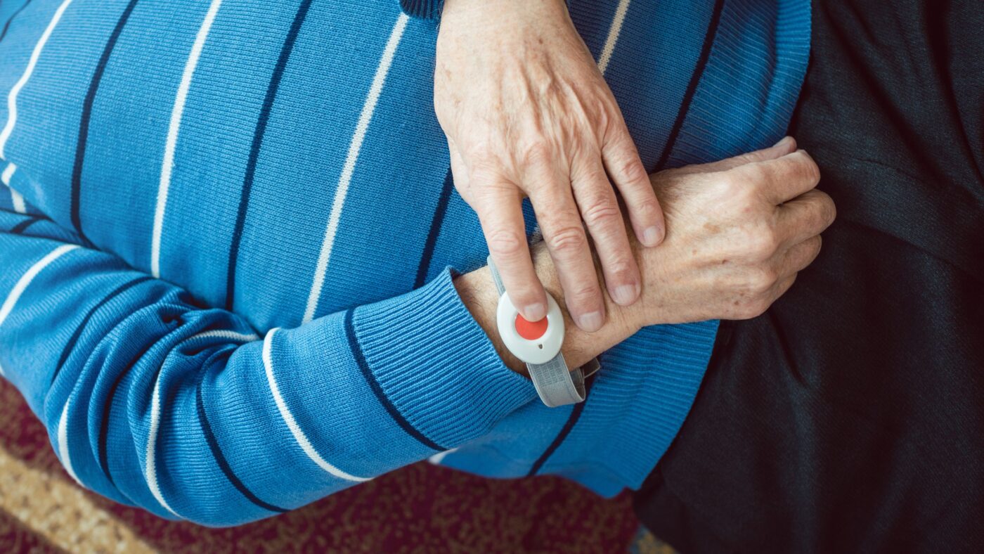 Ältere Person liegt auf dem Boden und drückt den Hausnotruf-Knopf am Handgelenk
