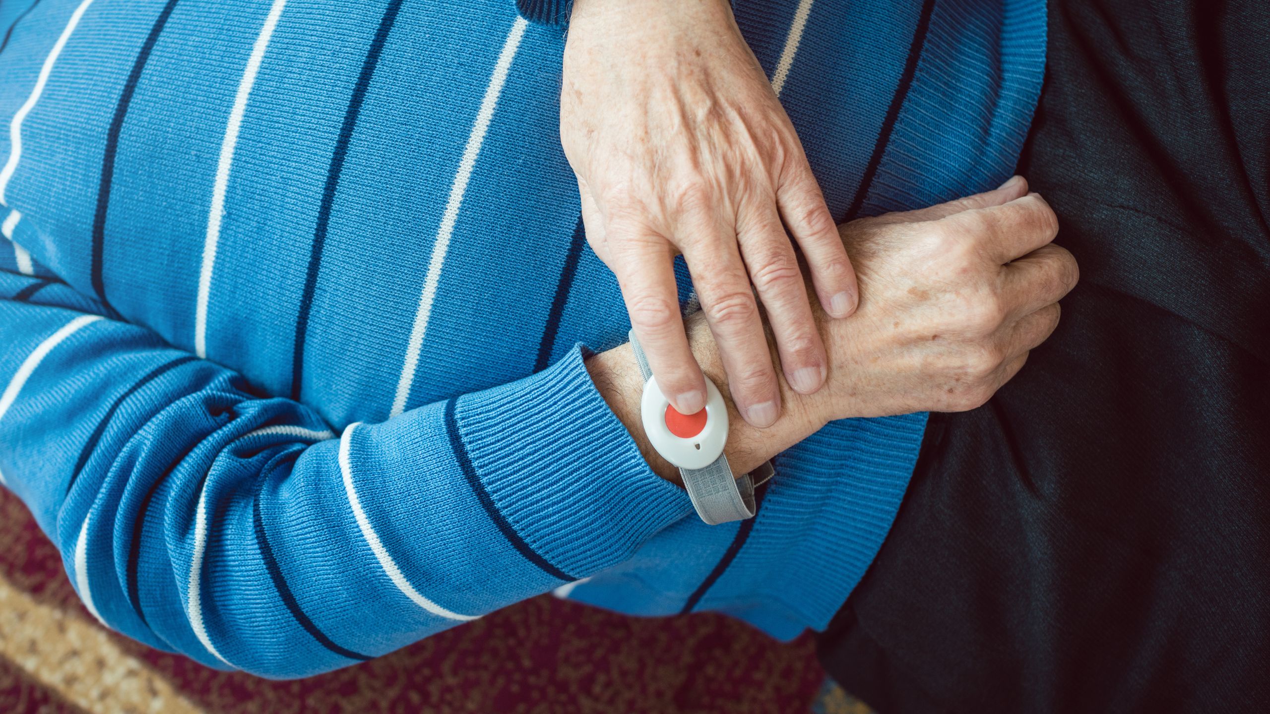 Ältere Person liegt auf dem Boden und drückt den Hausnotruf-Knopf am Handgelenk