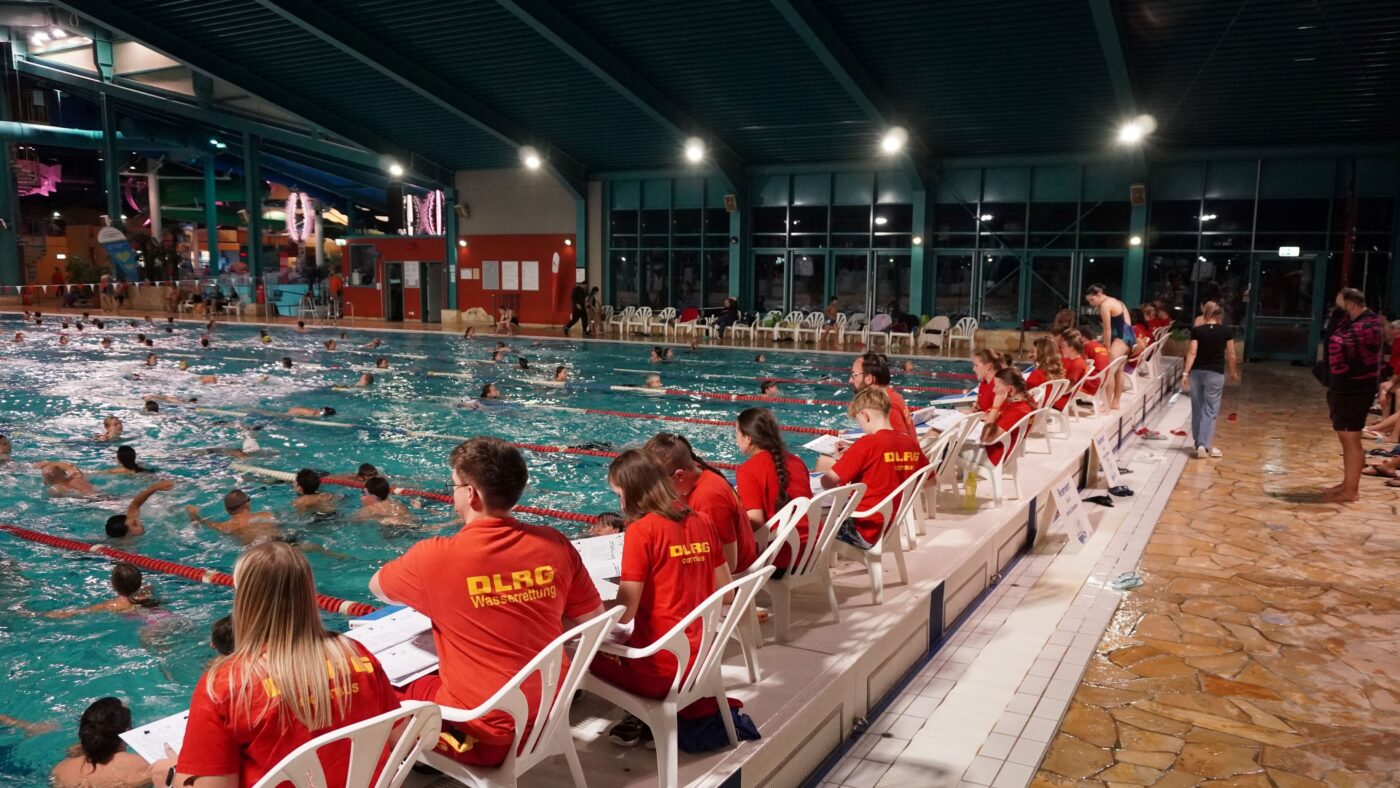 Das 24-Stunden-Schwimmen 2025 in der Cottbuser Lagune, die DLRG Ehrenamtlichen sitzen am Beckenrand und zählen die Runden der Teilnehmer