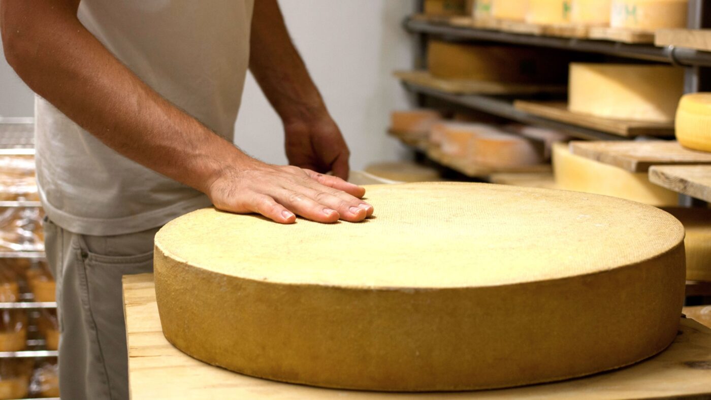 Ein Käser hat seine Hand auf einem Leib Käse