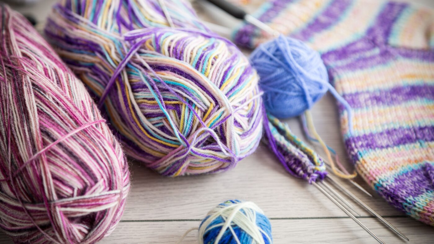 Gestrickte bunte Socken und Wolle liegen auf einem Holztisch