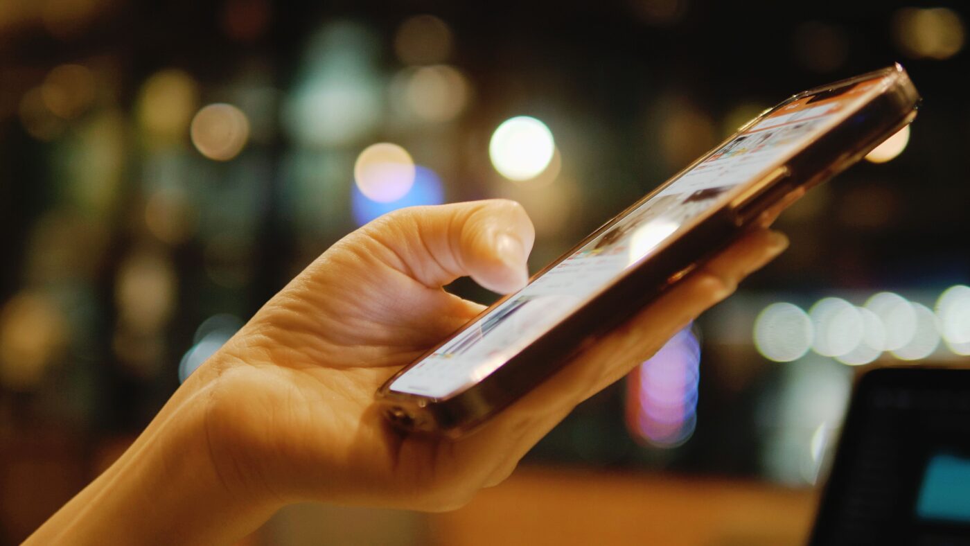 Ein Mensch hält ein Handy in seiner Hand und scrollt mit dem Daumen