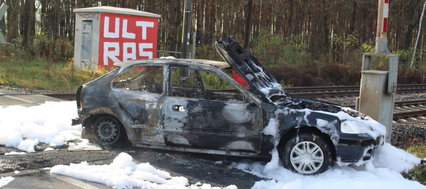 Ein vollkommen ausgebrannter PKW steht in Kolkwitz Krieschow von der Feuerwehr gelöscht mitten auf dem Bahnübergang in weißem Löschschaum