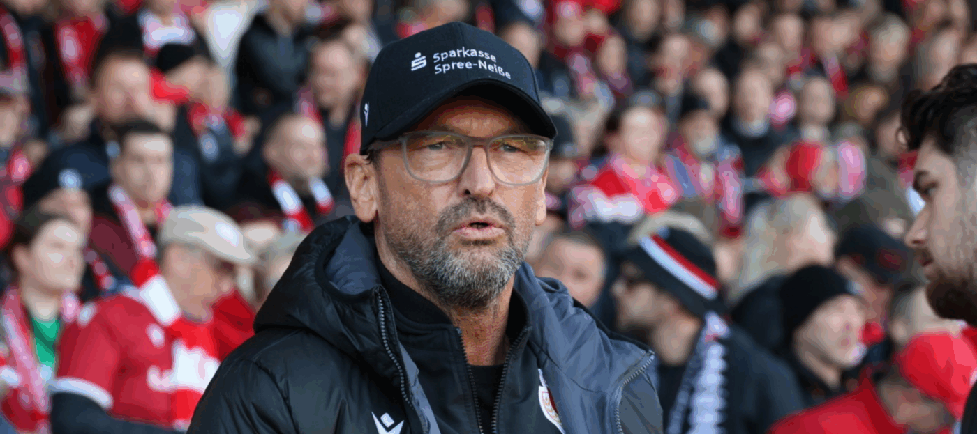 Der Trainer des FC Energie Cottbus Pele Wollitz steht vor der vollbesetzten Tribüne des LEAG Energie Stadions und schaut auf das Spielfeld