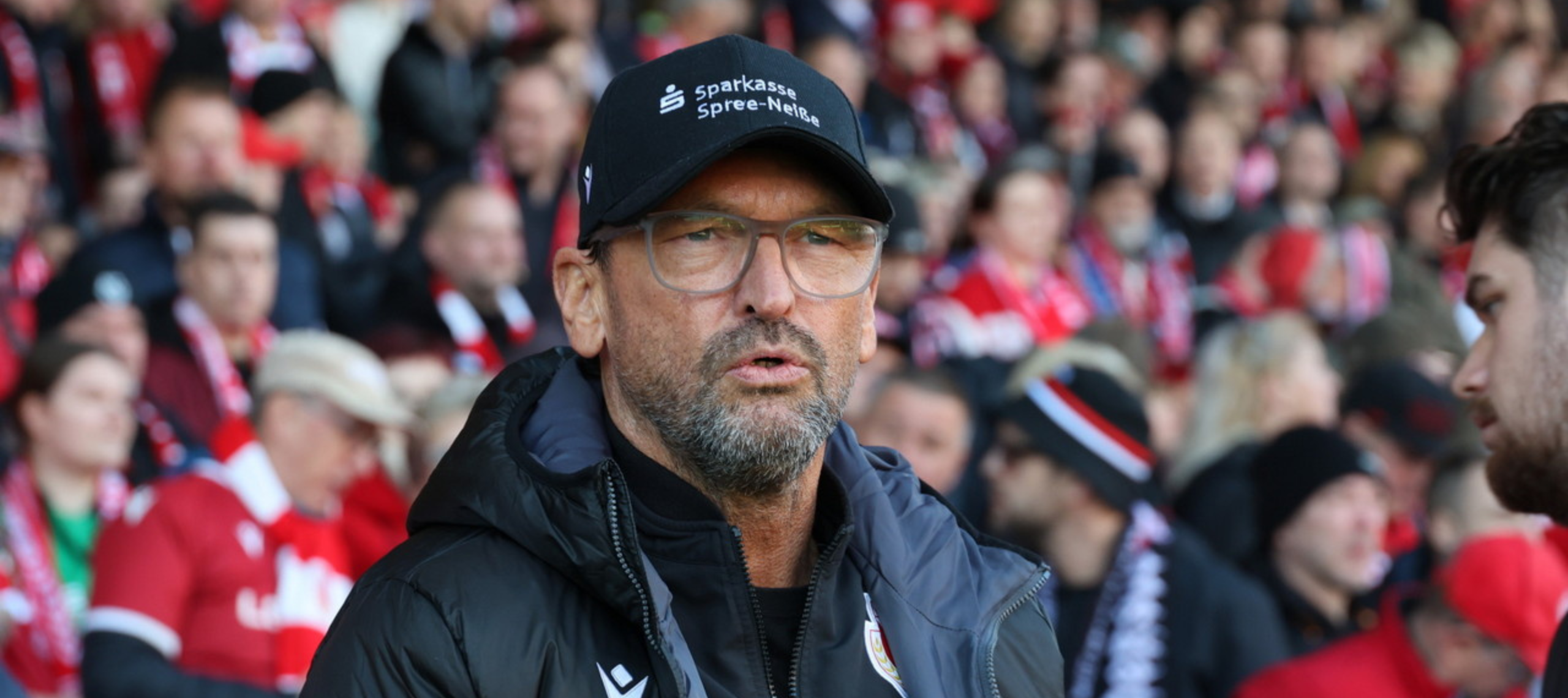 Der Trainer des FC Energie Cottbus Pele Wollitz steht vor der vollbesetzten Tribüne des LEAG Energie Stadions und schaut auf das Spielfeld