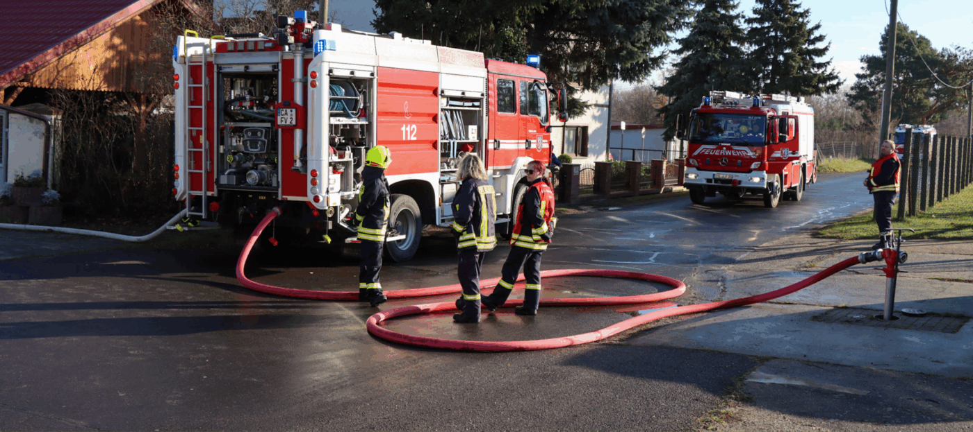 Löschwagen der Feuerwehr im Spreewald im Einsatz bei einem Werkstattbrand bei Spreewaldbauer Ricken mit Feuerwehrleuten rund um die Fahrzeuge und viele Schläuche auf dem Boden