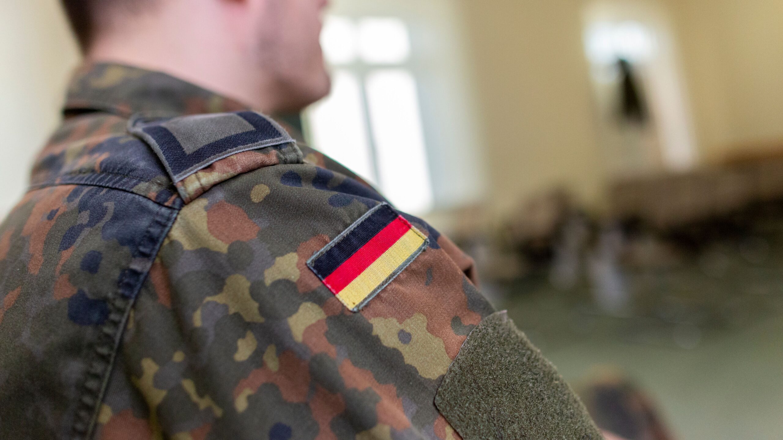 Ein Bundeswehrsoldat in Uniform in einem Klassenzimmer, auf seiner Uniform ist eine Deutschlandfahne