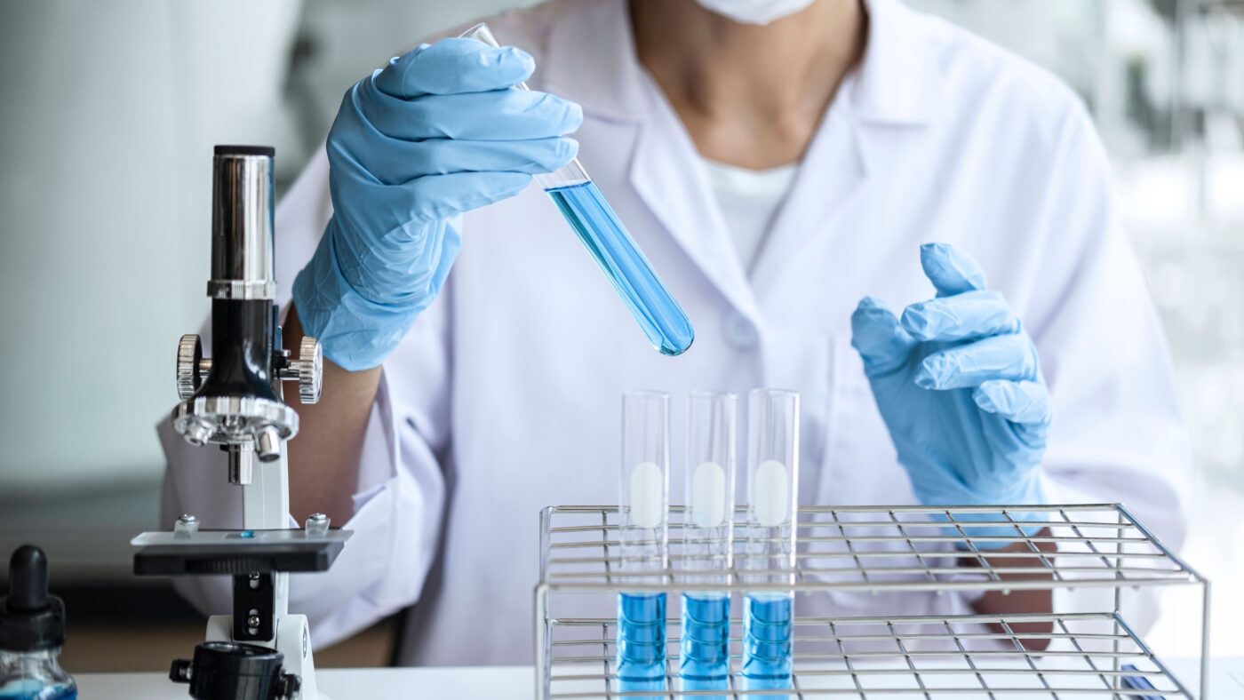 Eine Forscherin sitzt in einem Labor und hält ein Reagenzglas in der Hand