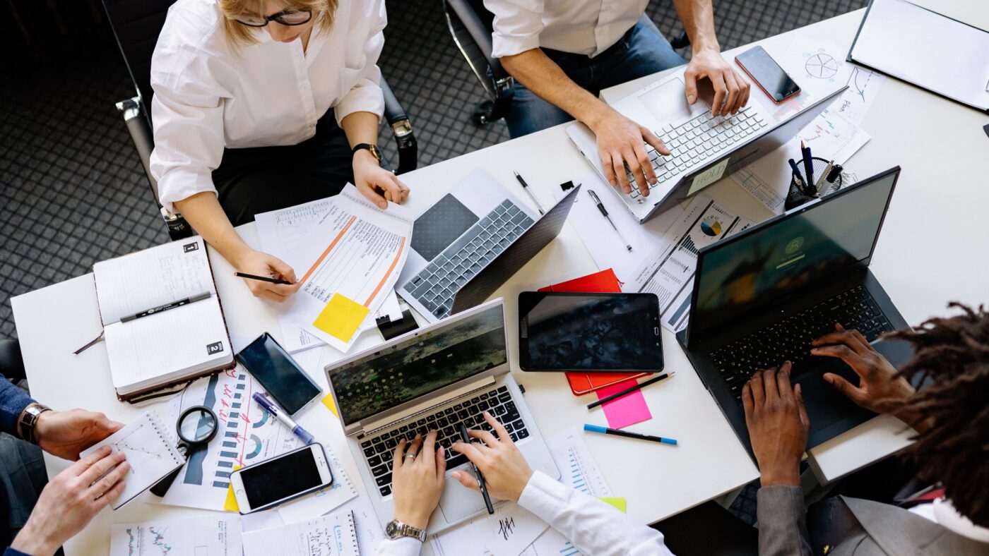 Ein Teammeeting, auf dem Tisch stehen viele Laptops und liegen Unterlagen und Statistiken