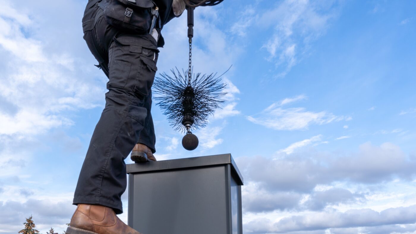 Ein Schornsteinfeger auf einem Dach, er hält die Bürste über dem kamin