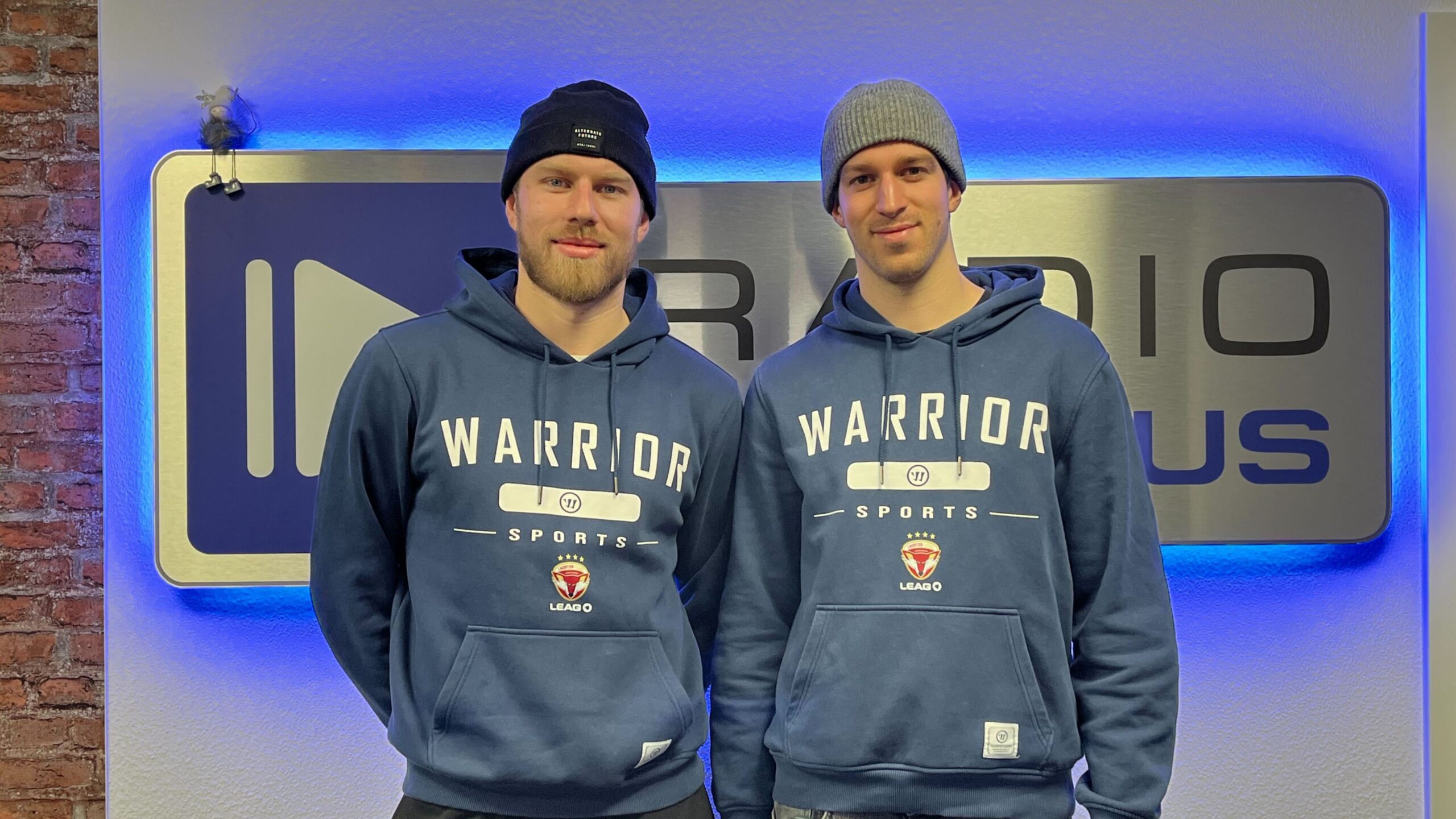 Die Lausitzer Füchse Spieler Tom Knobloch und Simon Stowasser vor dem Radio Cottbus Logo