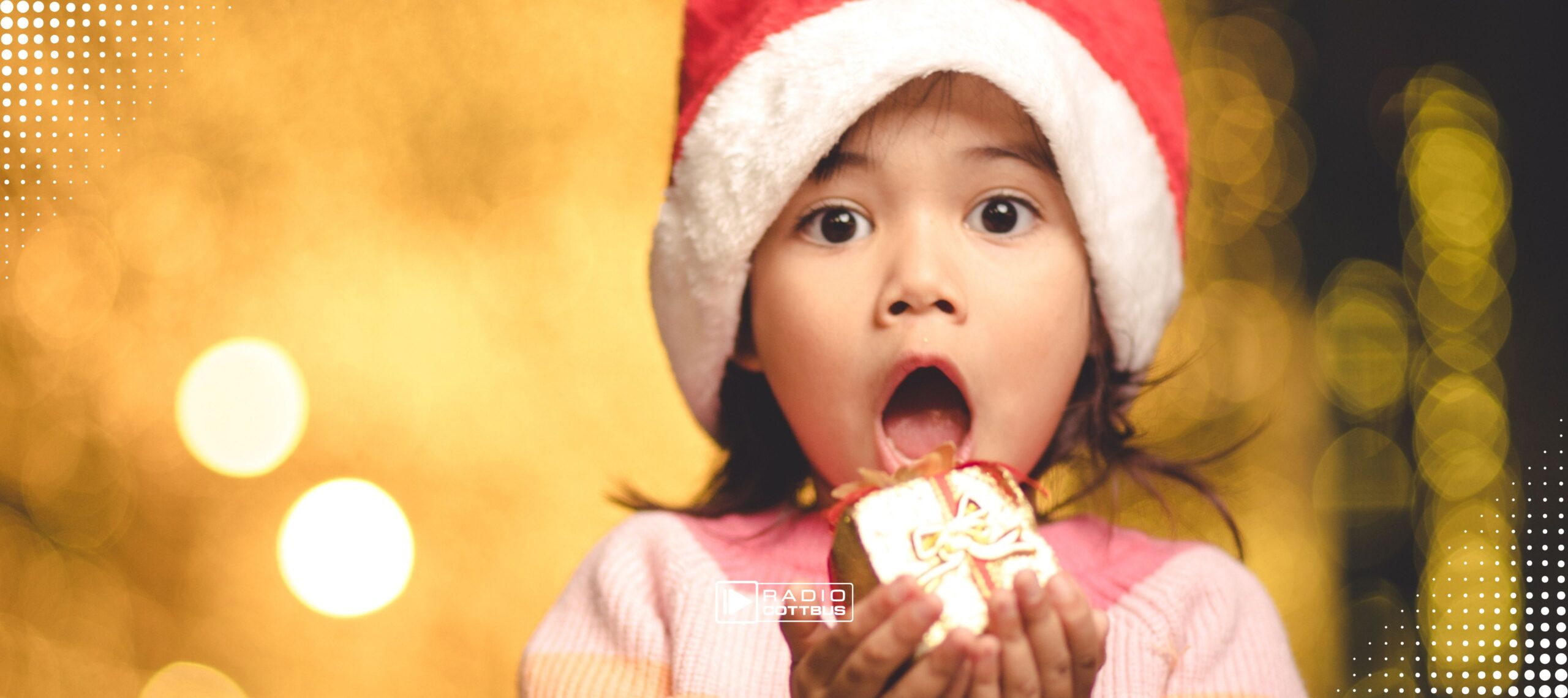 Ein staunendes Kind in der Weihnachtszeit hält vor einem goldenen Hintergrund ein kleines Geschenk in den Händen und hat den Mund vor Staunen geöffnet