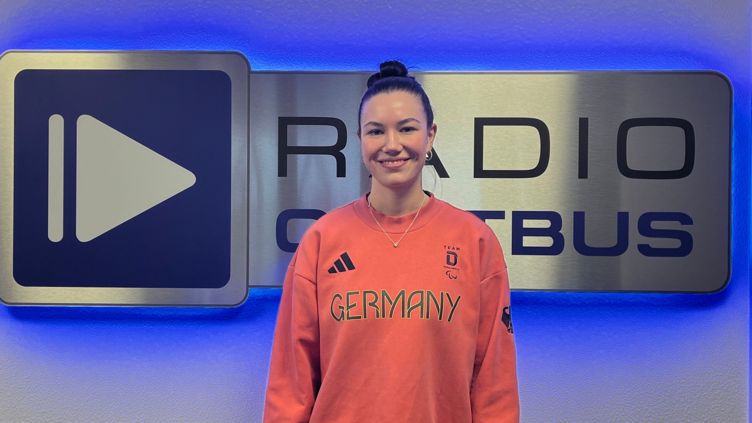 Paula Kohlstock vom paralympischen Stützpunkt Cottbus vor dem Radio Cottbus Logo