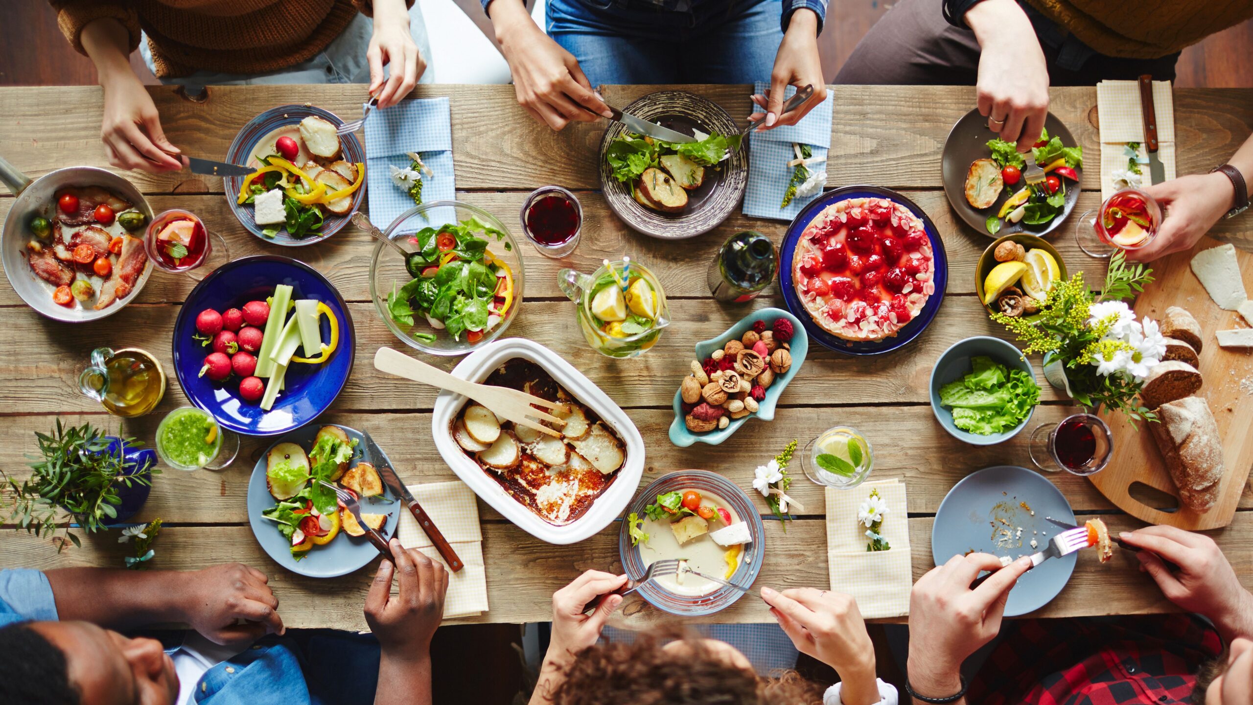 Ein Essenstisch von oben fotografiert an dem sechs Personen sitze und auf dem mehrere Speisen stehen