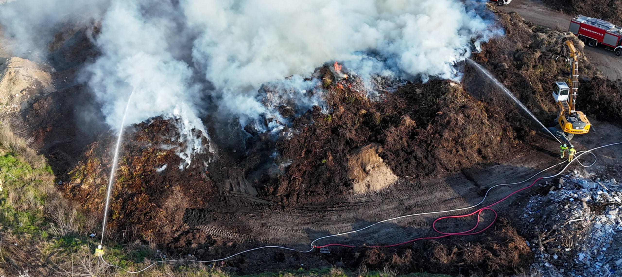 Auf dem Gelände der ALBA Cottbus gibt es einen Brand in einem großen Abfallhaufen und die Feuerwehr löscht, während viel weißer Rauch aufsteigt