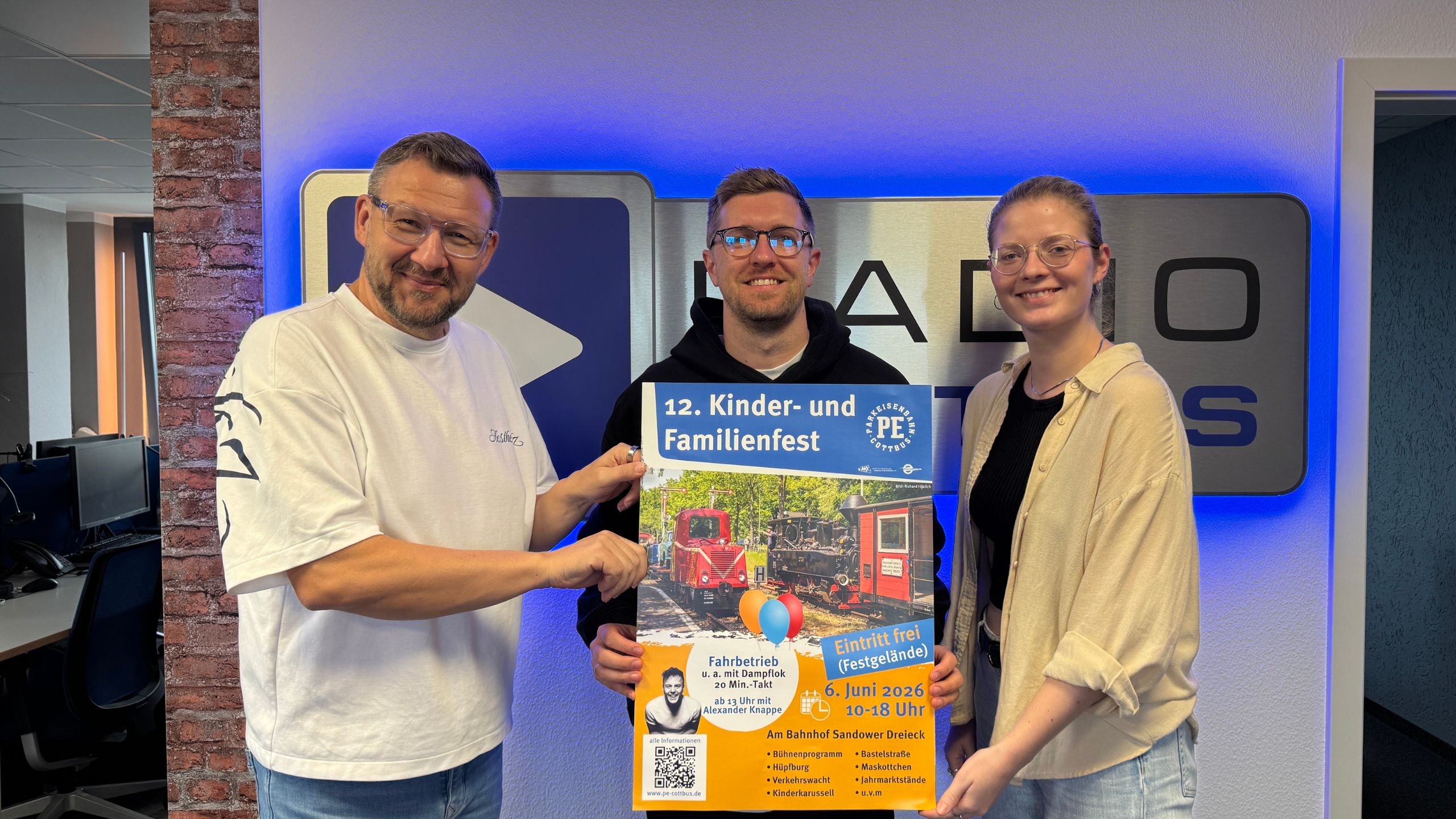 Die Wacher Macher Ronny Gersch und Luka Stadelmeier vor dem Radio cottbus Logo gemeinsam mit Udo Seidel von Cottbus Verkehr