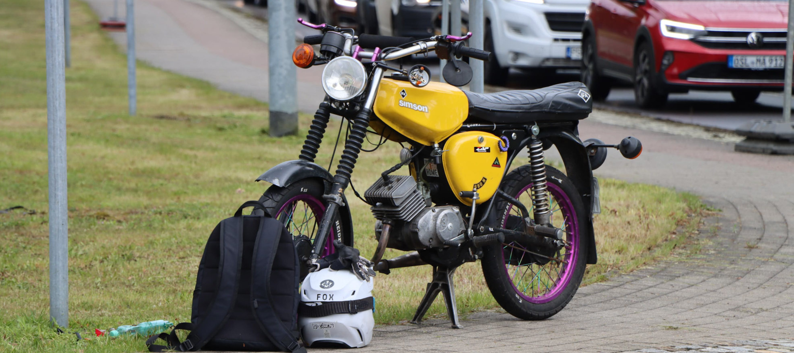 Die gelbe Simson mit violetten Felgen eines Jugendlichen in Ruhland steht nach einem Unfall am Straßenrand. Davor stehen der Rucksack und der Helm, nachdem ein Auto auf die leicht beschädigte Simson aufgefahren ist. Der Lenker ist leicht verbogen.