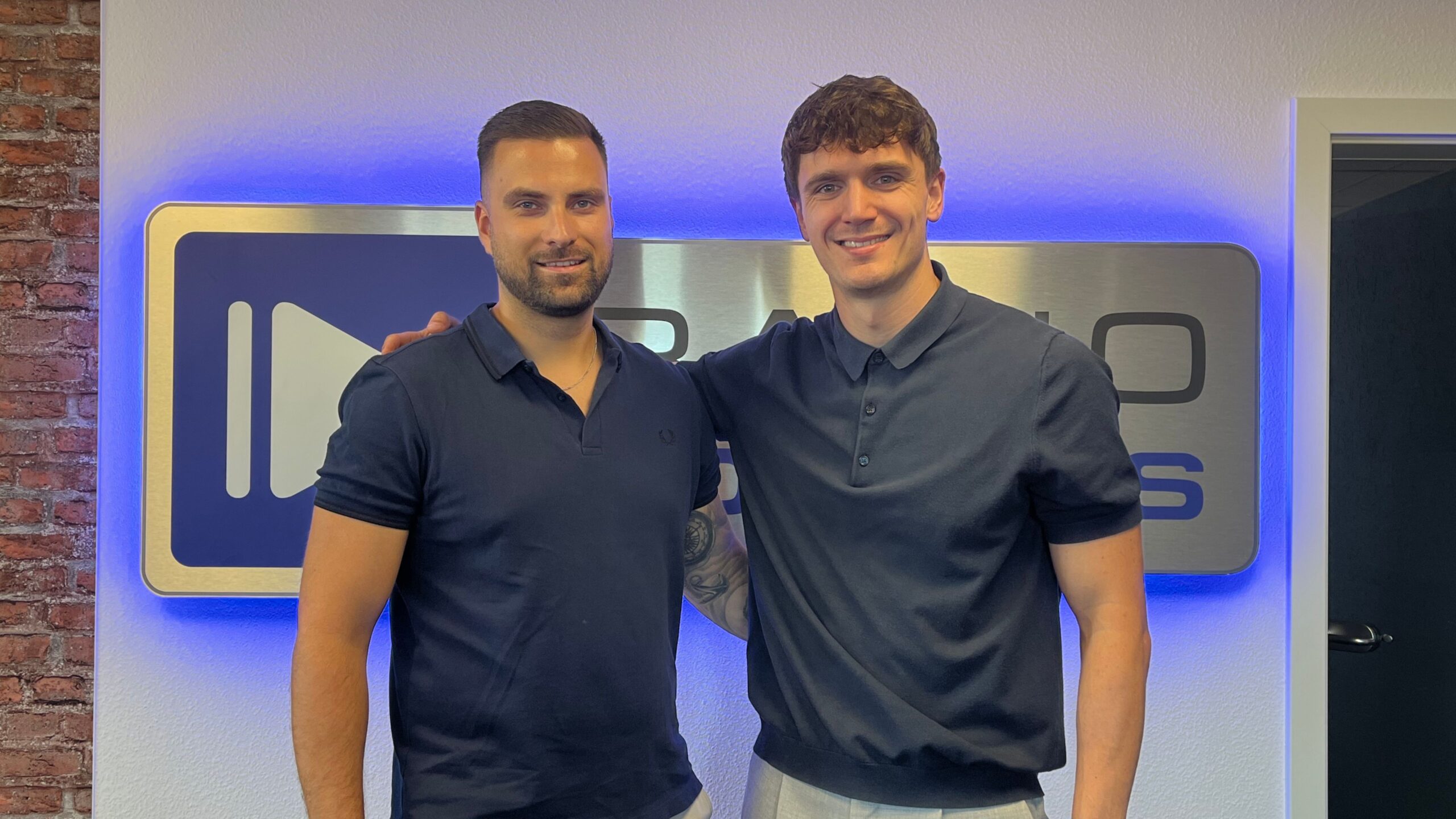 Eric Bäse und Theo Zastrau von Bäse Consulting vor dem Radio Cottbus Logo