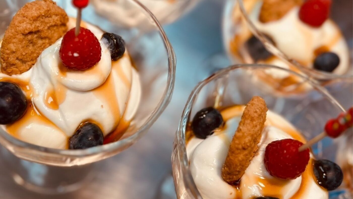 Mehrere Sahnedesserts in Gläsern mit Früchten und Keksen obendrauf