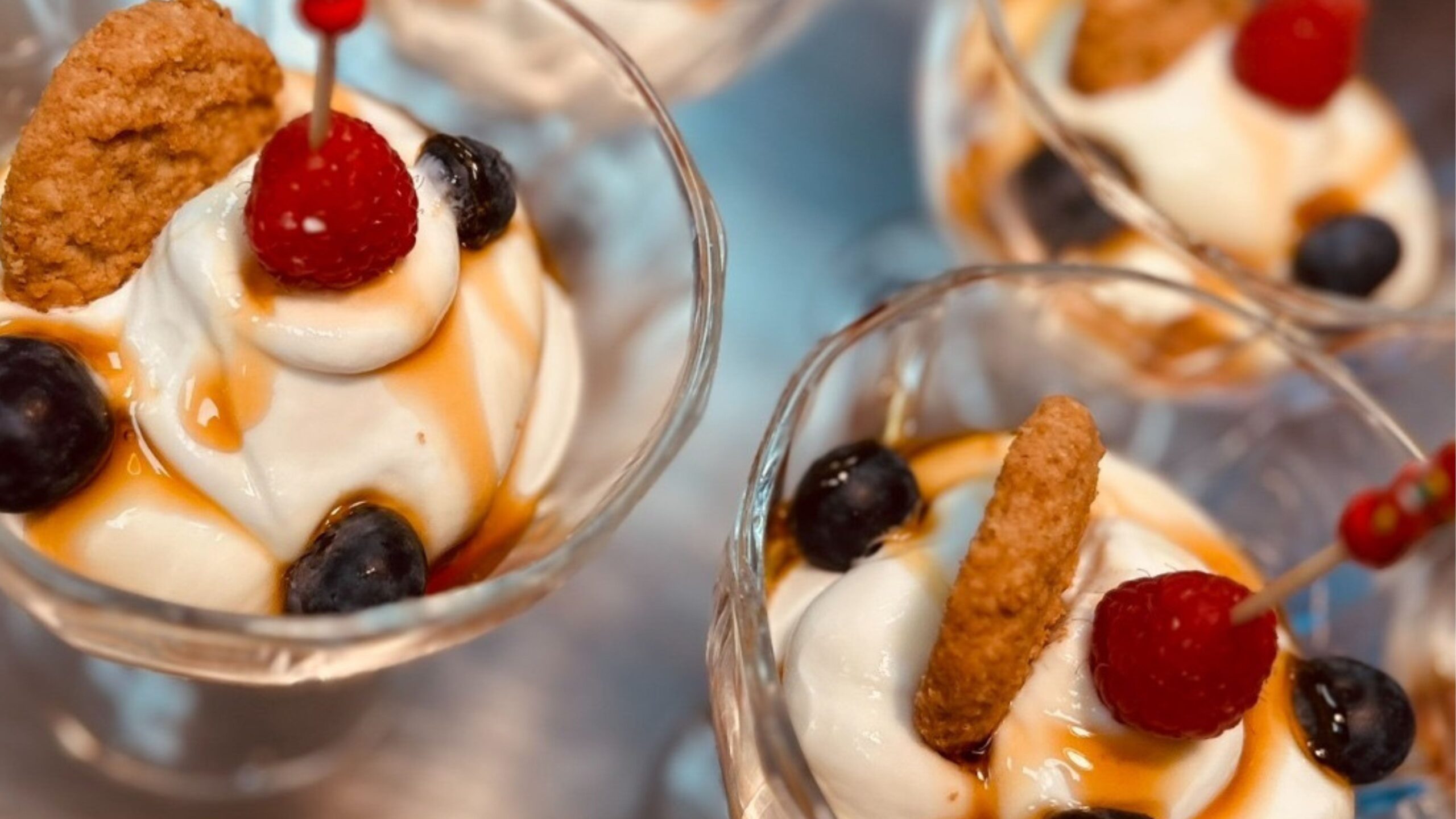 Mehrere Sahnedesserts in Gläsern mit Früchten und Keksen obendrauf