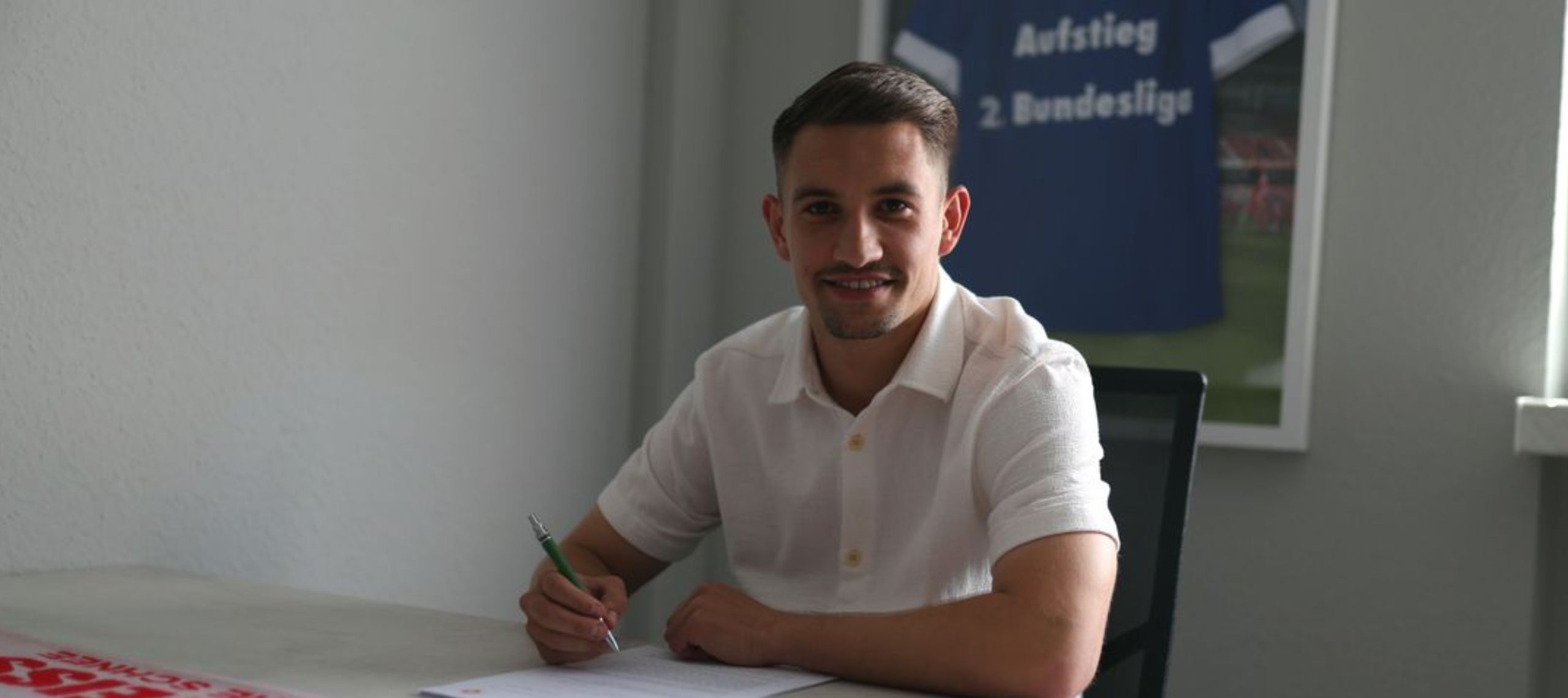 Julian Guttau unterschreibt seinen neuen Vertrag beim FC Energie Cottbus und lächelt nach seinem Wechsel vom FC Erzgebirge Aue in die Kamera