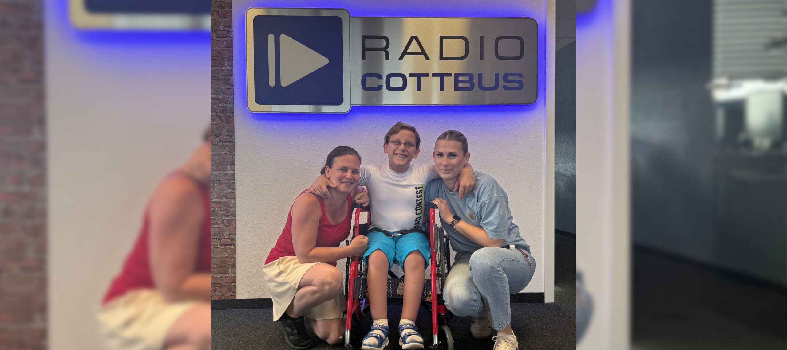 Egon aus Cottbus (Mitte), mit seiner Mutter Susi (links) und seiner Cousine Josefine (rechts) vor dem Radio Cottbus Logo
